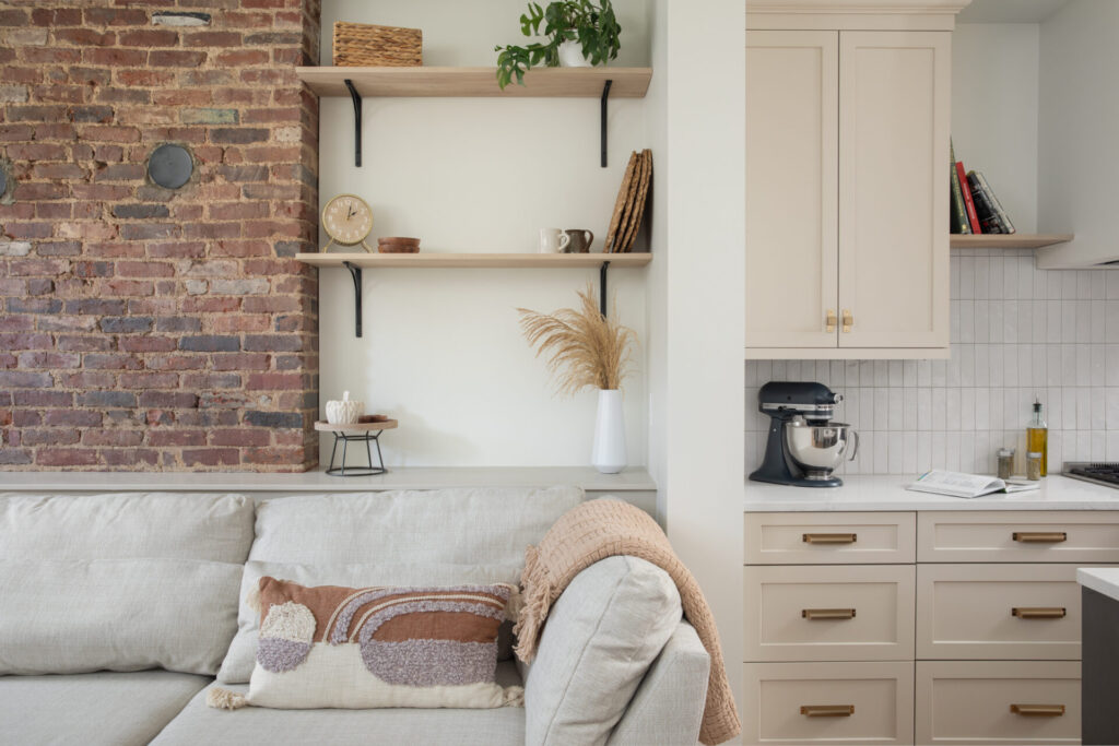 A couch with a brick chimney in the background, shelving nearby, and the kitchen within view